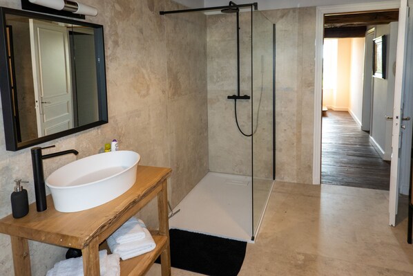 A bathroom with a large white sink, a wooden vanity, a glass shower enclosure, and a mirror above the sink. - La Maison de Souhey (Souhey)