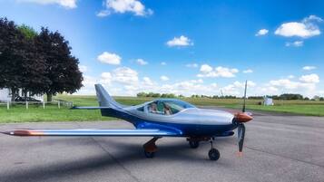 Un petit avion bleu et blanc est garé sur une piste, avec un champ herbeux et des arbres en arrière-plan.