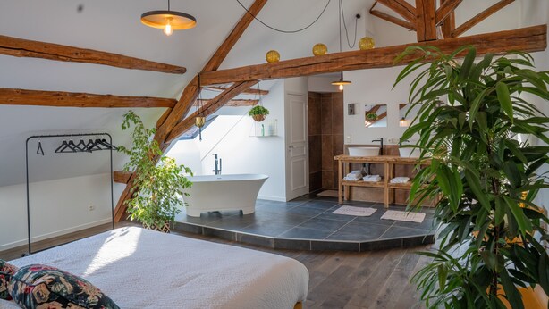 Un dormitorio con una cama grande, techo de madera, baño y un pequeño rincón de descanso.