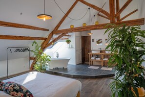 Un dormitorio con una cama grande, techo de madera, baño y un pequeño rincón de descanso.