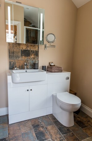 A bathroom with a white vanity, a round mirror, a toilet, and a decorative tile backsplash. - Charlestown Retreat Apartment (St Austell)