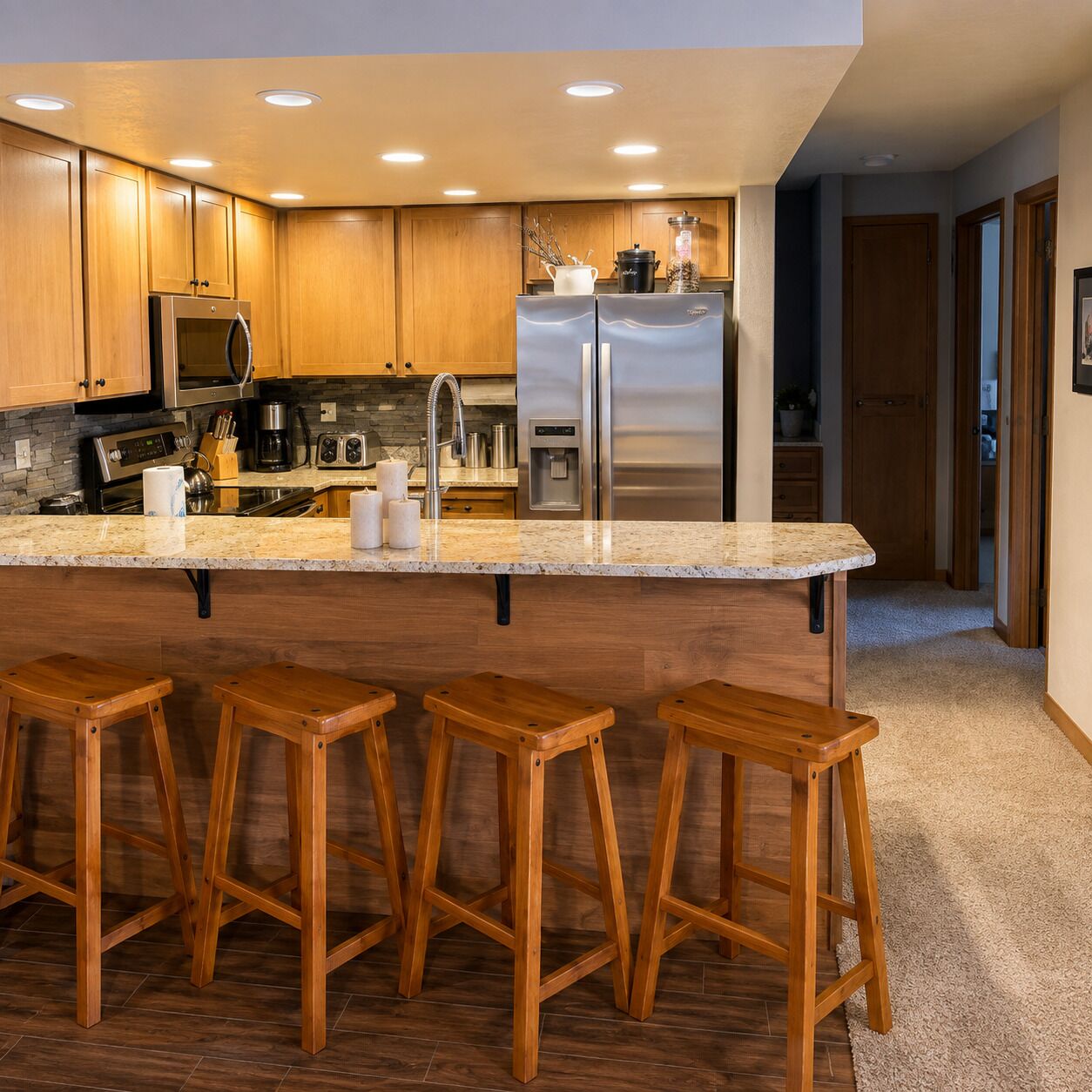 Una cocina moderna con armarios de madera, electrodomésticos de acero inoxidable, encimera de granito y taburetes de bar de madera.
