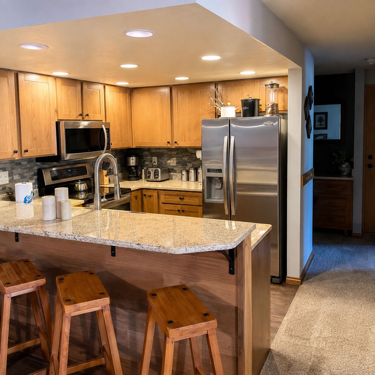 Una cocina moderna con gabinetes de madera, electrodomésticos de acero inoxidable, encimeras de granito y taburetes de madera.