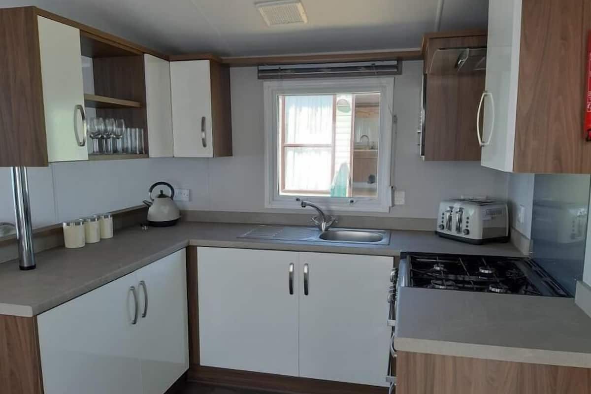 A compact kitchen with white cabinets, a gas stove, a sink, and a toaster.