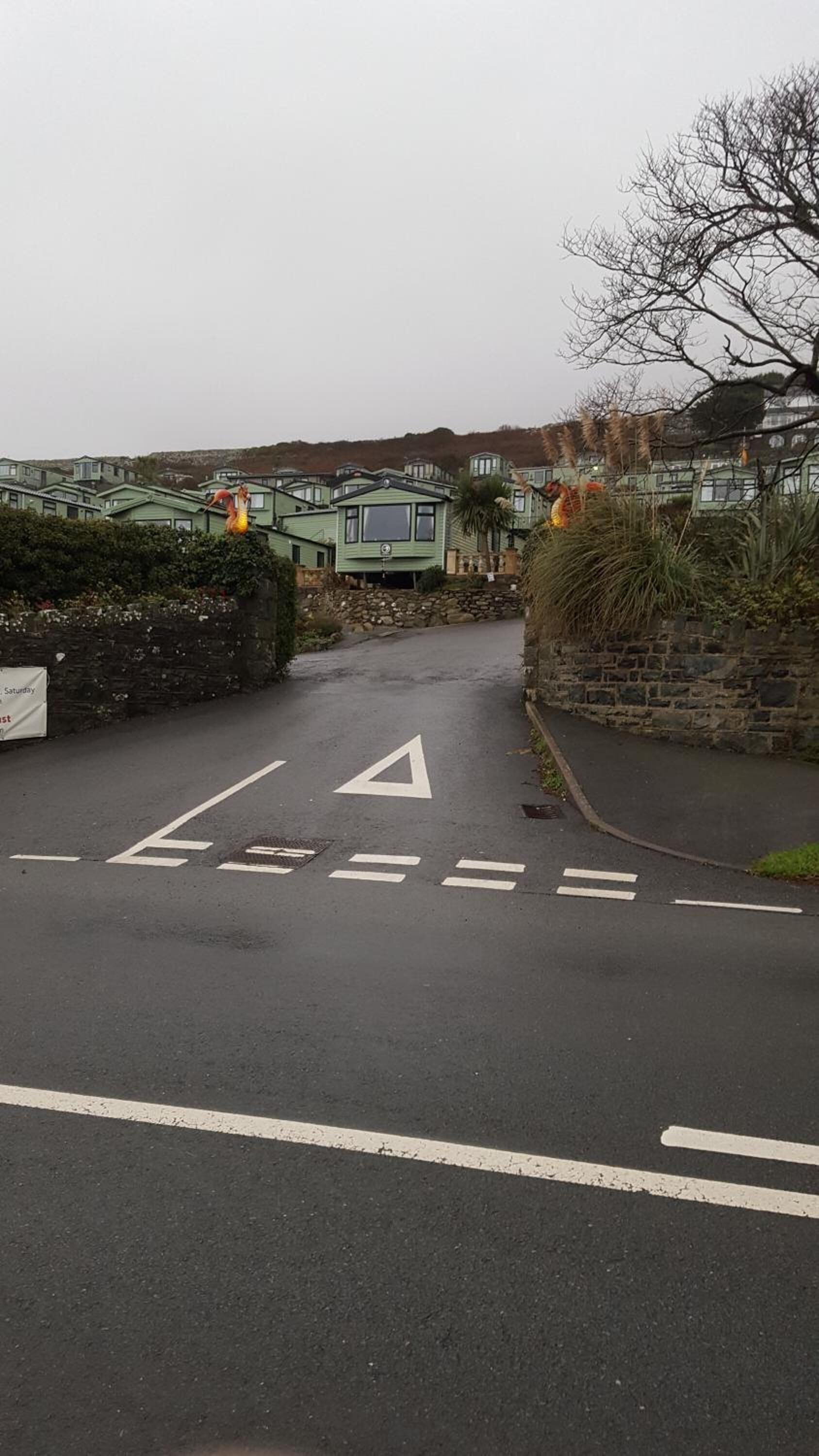 A road leading to a residential area with houses and a stone wall.