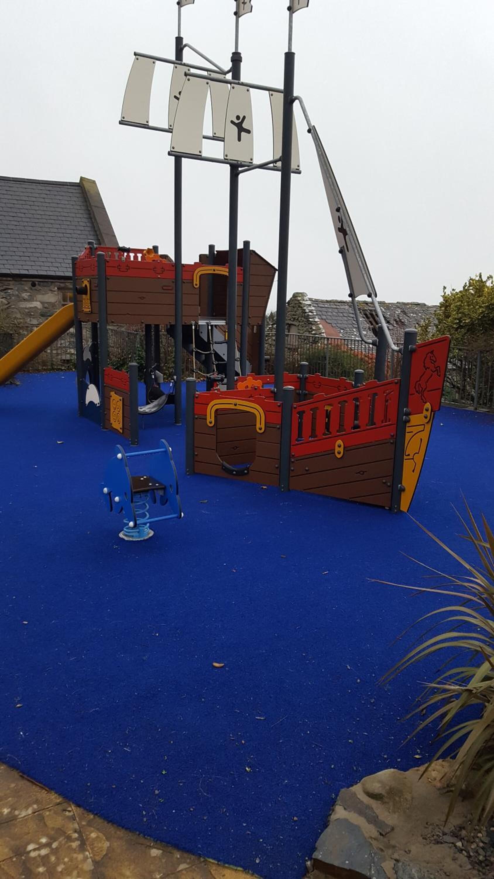 A children's play area with a pirate ship play structure, a slide, and a climbing frame.