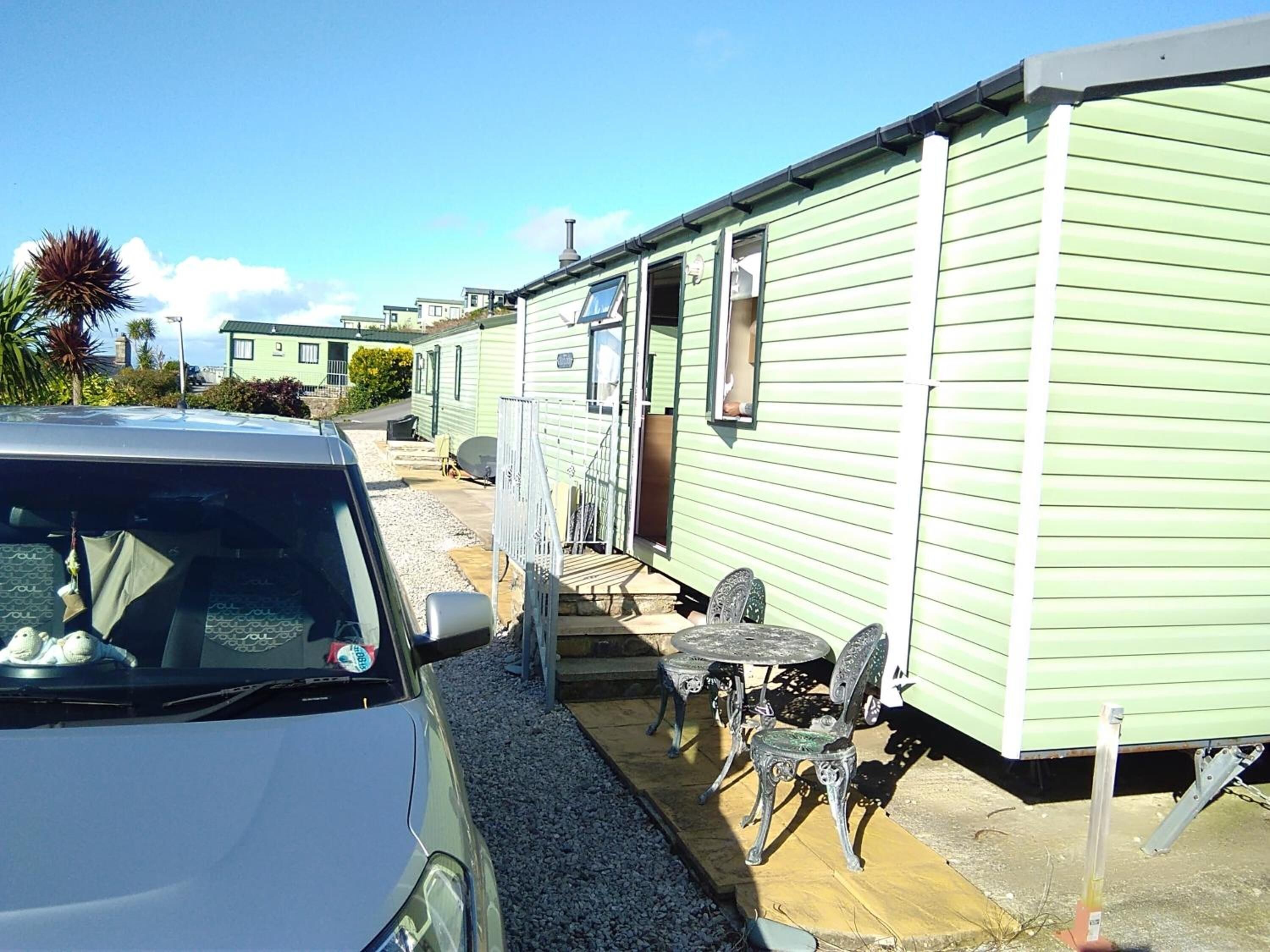 Une maison mobile avec une voiture garée devant, du mobilier d’extérieur et un ciel dégagé.