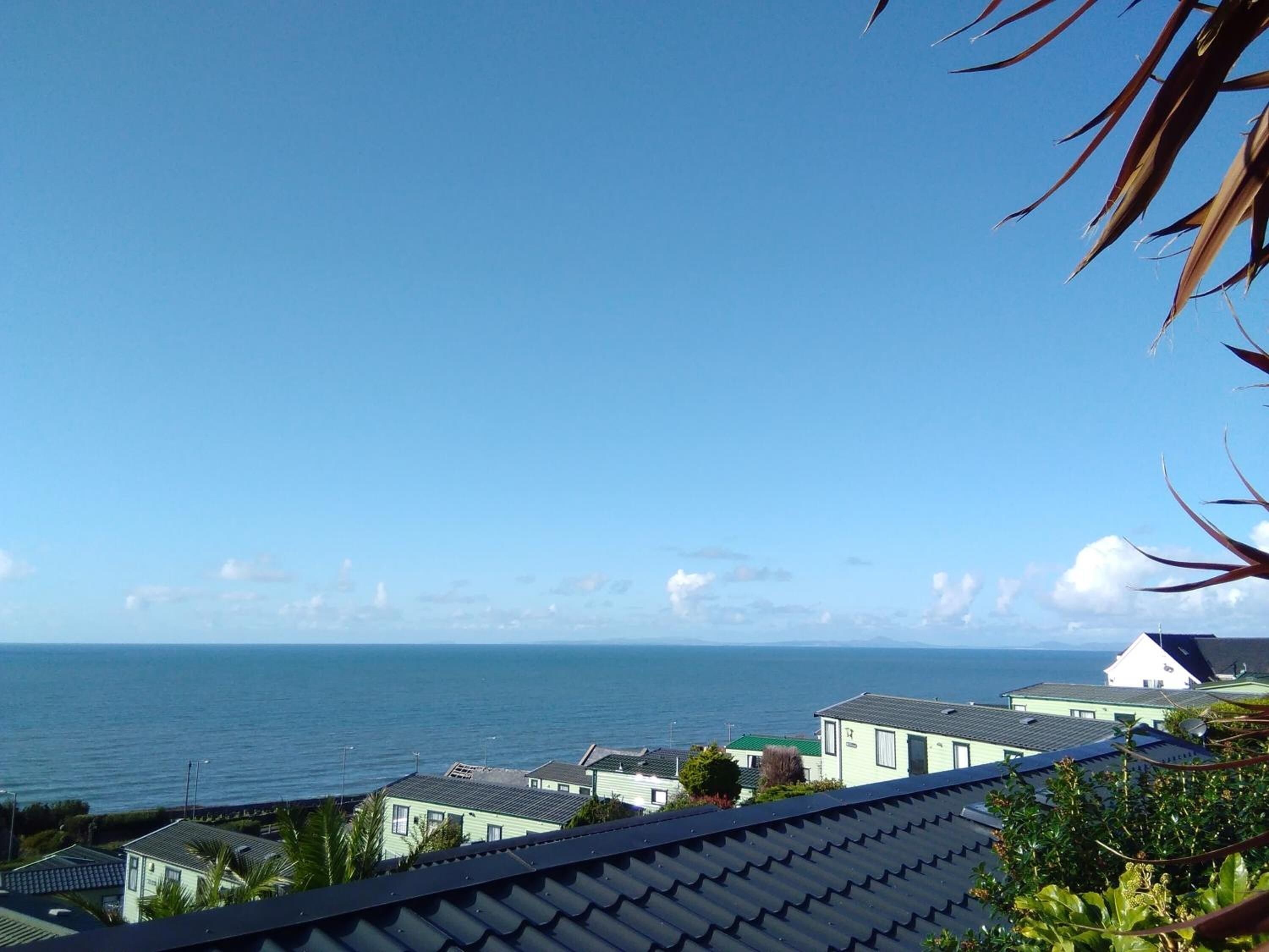 Vista costera con cielo despejado, masa de agua y varios edificios con techo inclinado.