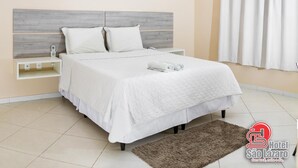 A neatly arranged bedroom with a bed, bedside tables, a wall-mounted air conditioner, and a window with curtains. - Hotel São Lázaro (Brumado)