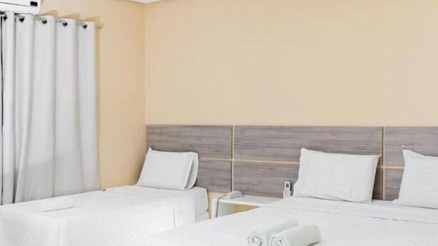 A hotel room with two beds, a bedside table with a phone, and a rolled towel on the bed. - Hotel São Lázaro (Brumado)
