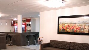 A modern living room with a brown sofa, a glass coffee table with decorative items, and a painting of tulips on the wall. - Hotel São Lázaro (Brumado)
