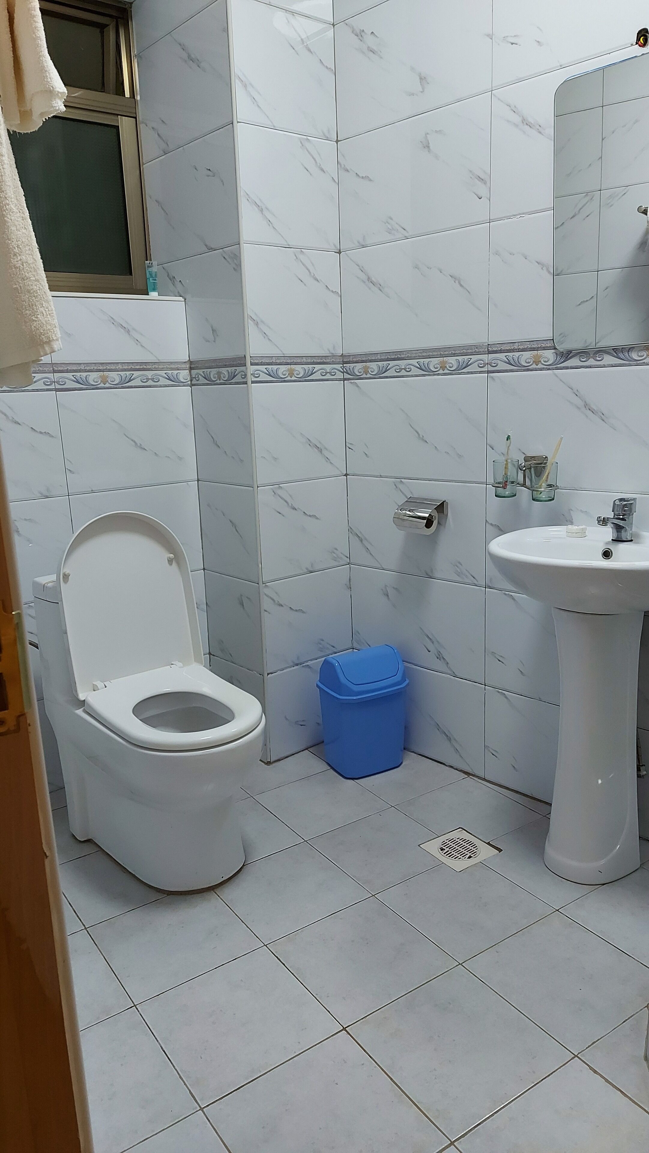 A bathroom with a toilet, sink, and blue trash bin.