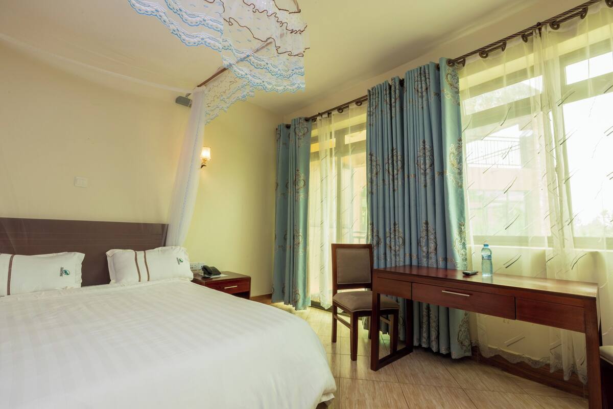 Quarto de hotel com cama, escrivaninha, cadeira e cortinas.