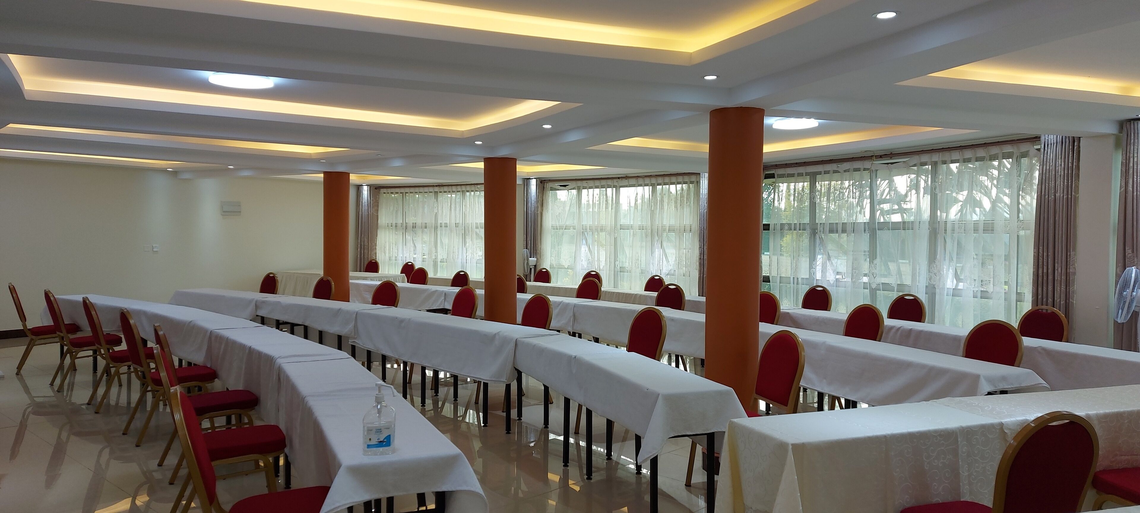 A conference room with long tables, red chairs, and large windows with curtains.