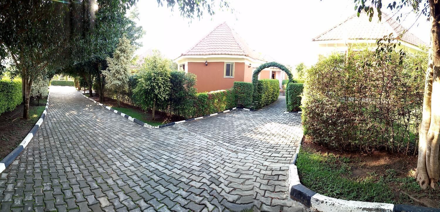 Un sendero pavimentado que conduce a un edificio con techo rojo, rodeado de setos y árboles bien cuidados.