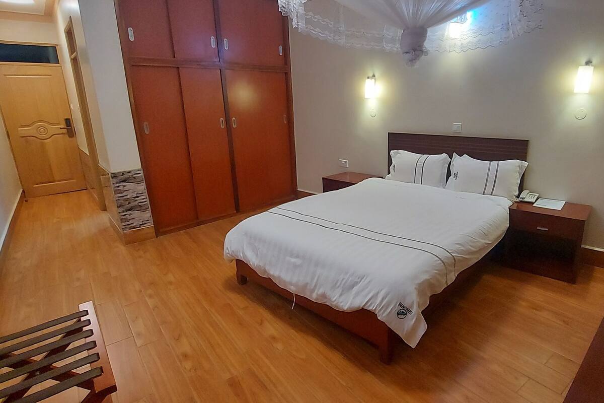 Quarto com cama, guarda-roupa de madeira, mesas de cabeceira e um criado-mudo.