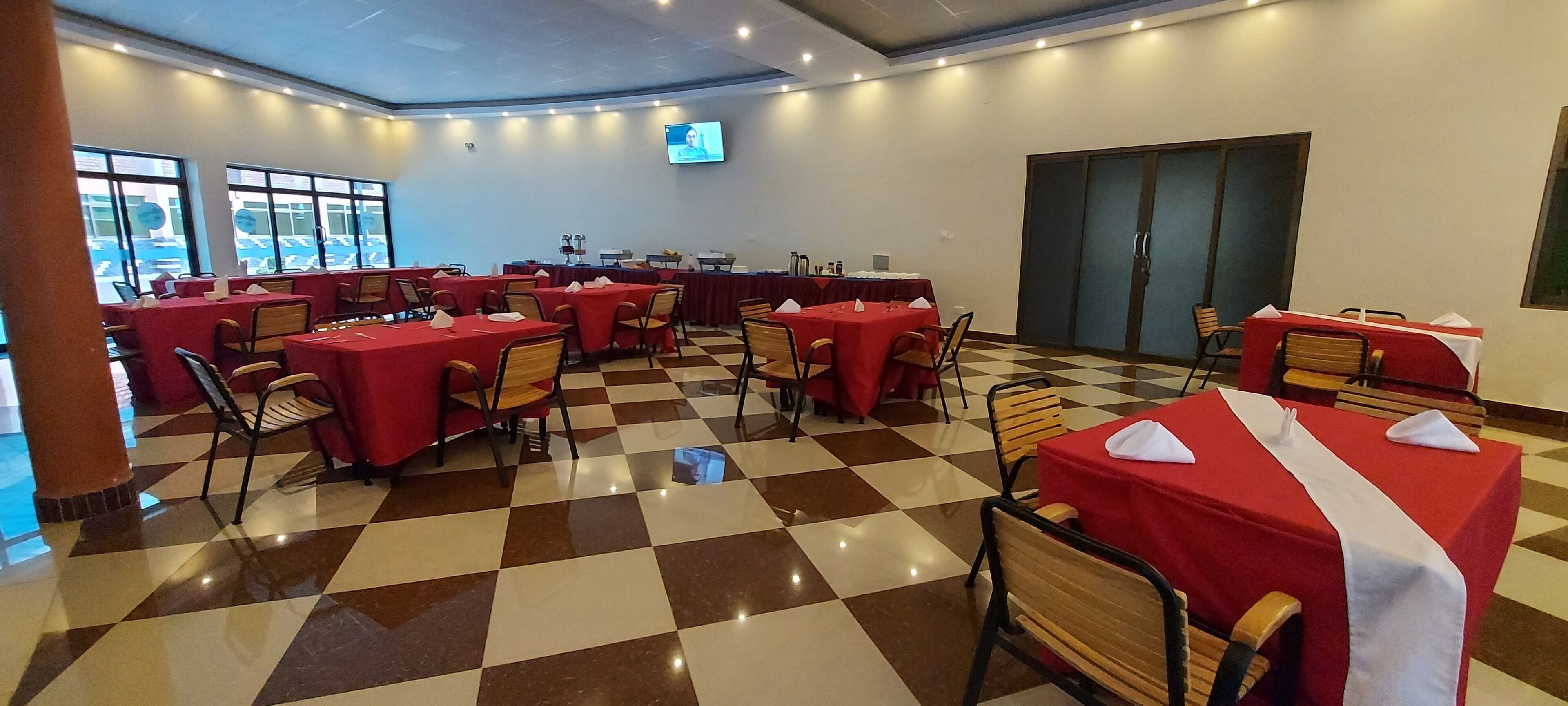 Un salón de conferencias con mesas cubiertas de manteles rojos, sillas y una pantalla de televisión.