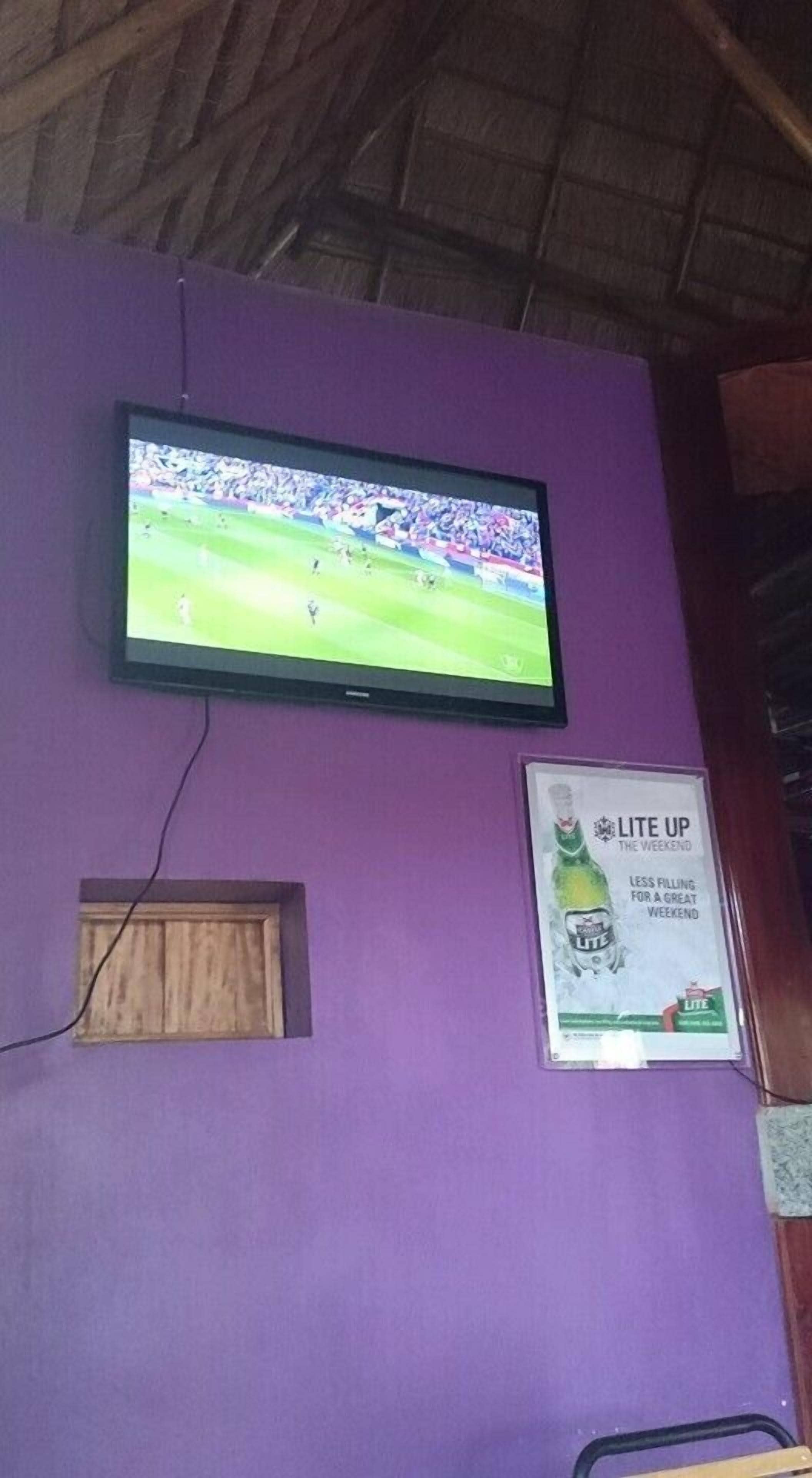 A television mounted on a purple wall with a poster advertising 'LITE UP THE WEEKEND'.