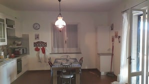 A compact kitchen with white cabinets, a dining table with chairs, a hanging light fixture, and a window with curtains. - Cozy vacation home on a farm, Bagno di Gavorrano, Tuscany (Bagno di Gavorrano)