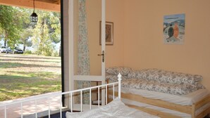 A bedroom with a wooden bed, a floral-patterned sofa, a door with a floral curtain, and a painting on the wall. - Cozy vacation home on a farm, Bagno di Gavorrano, Tuscany (Bagno di Gavorrano)