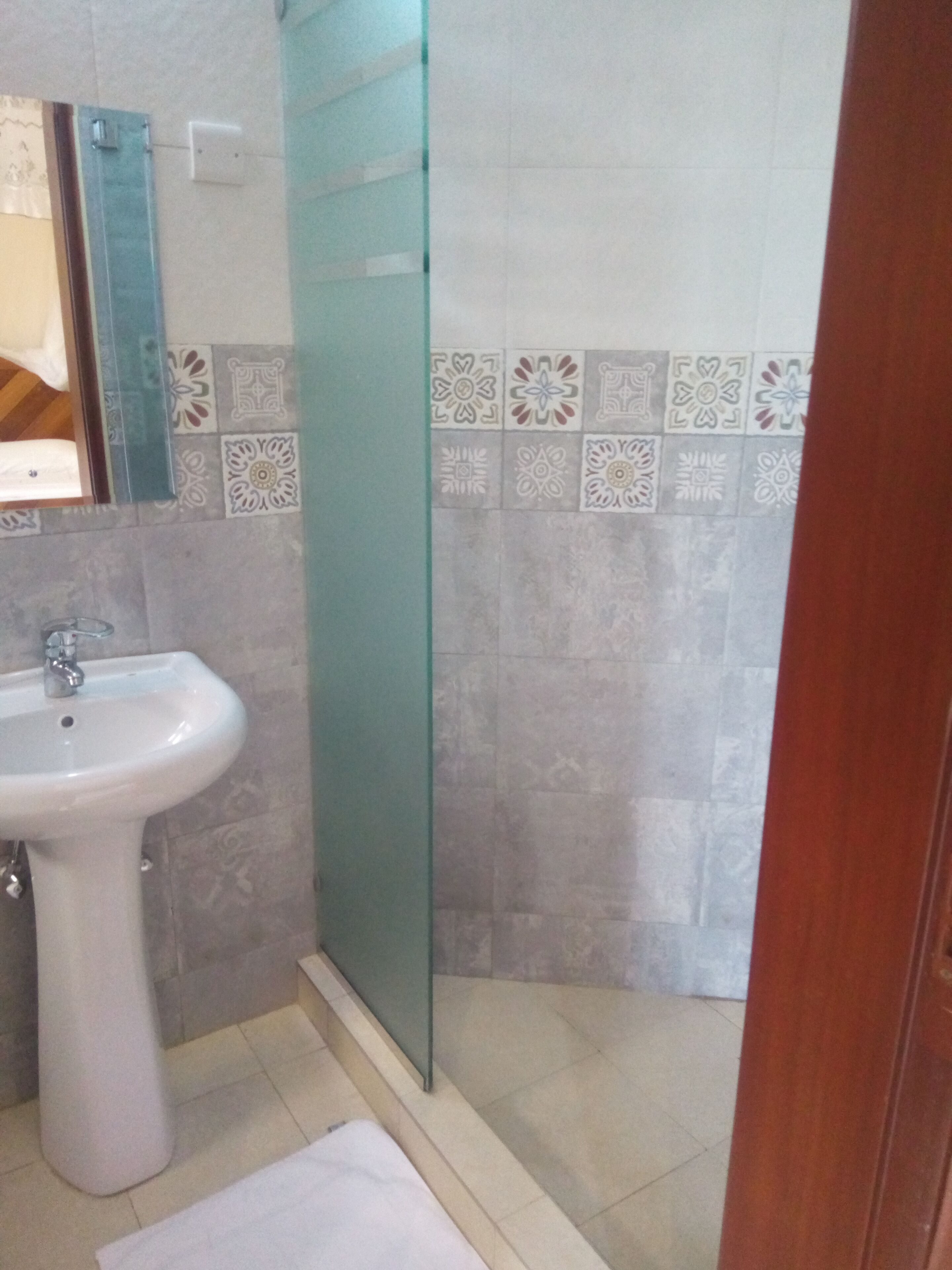 Een badkamer met een wit wastafelmeubel, een douchecabine van glas en decoratieve tegels op de muren.