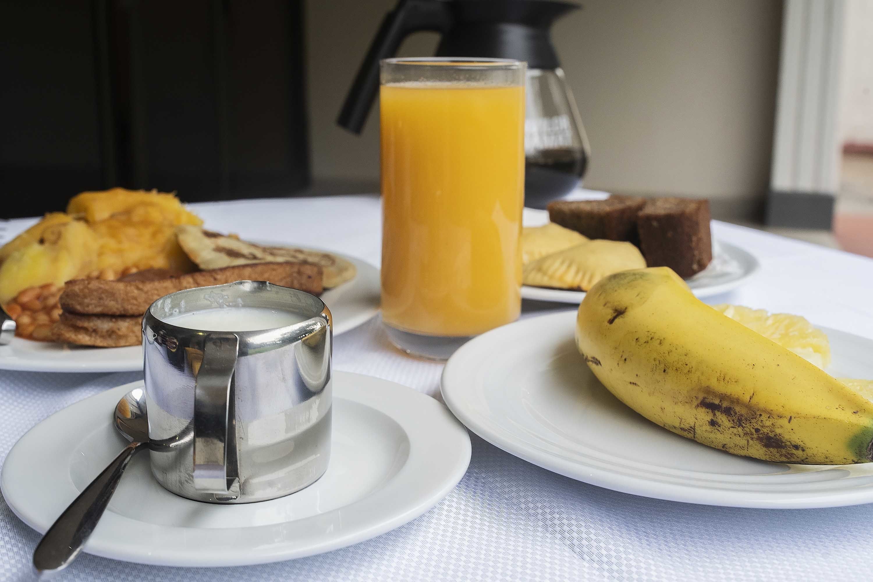 A breakfast table with plates of food, a glass of orange juice, and a metal container.