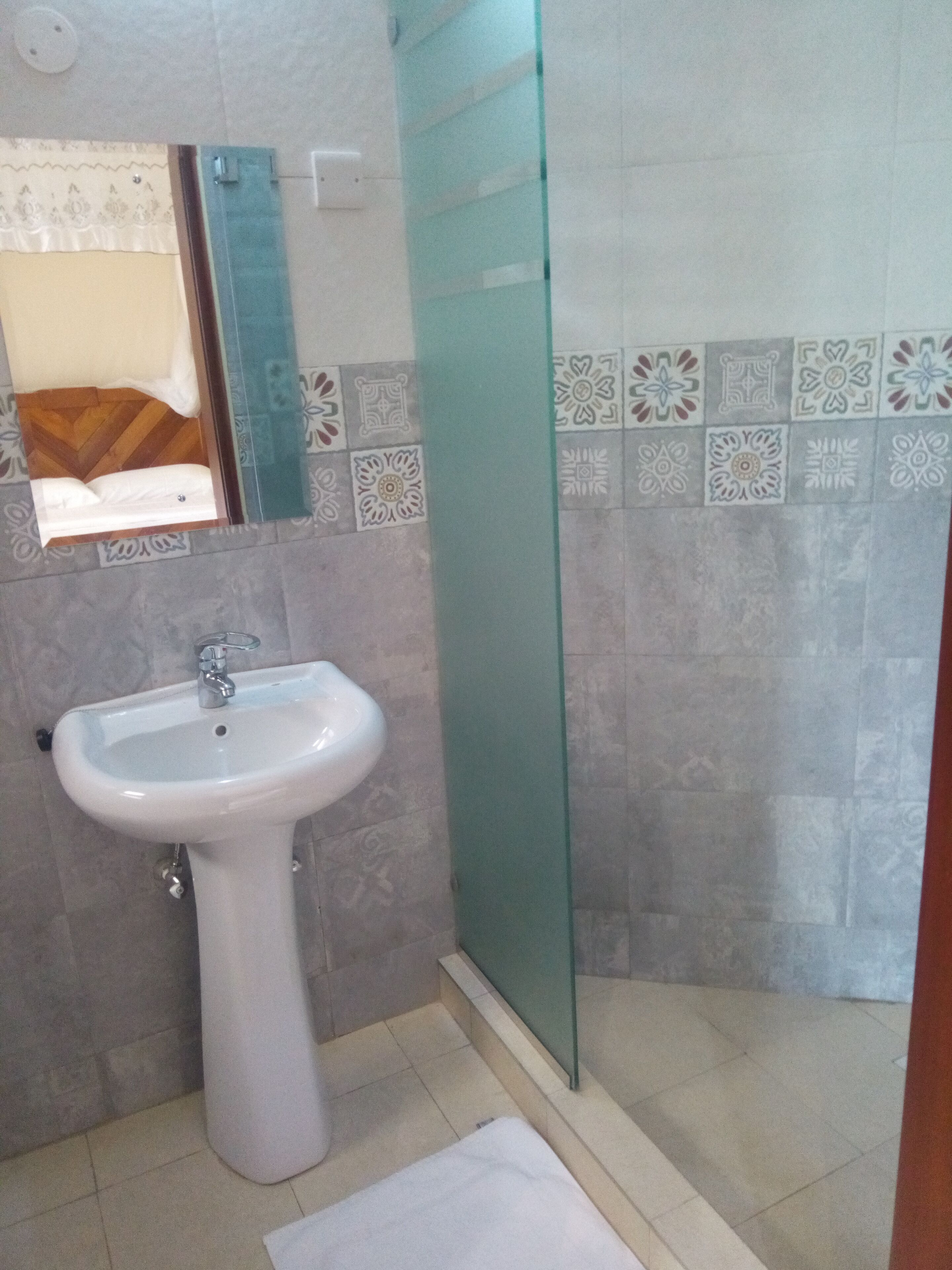 A bathroom with a pedestal sink, a glass shower enclosure, and patterned tiles on the walls.