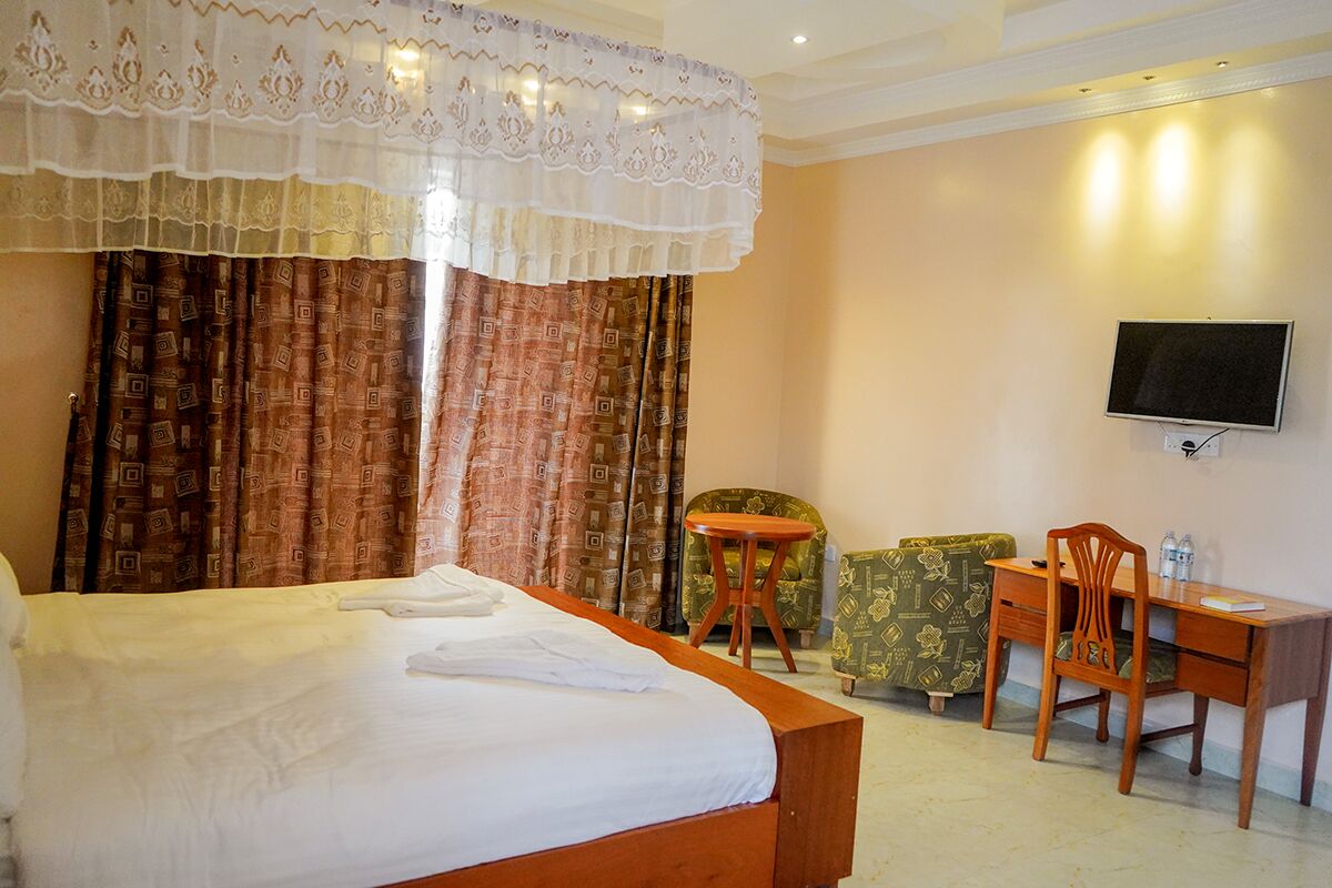 Habitación de hotel con una cama grande, un escritorio, una silla, un televisor y cortinas estampadas.