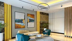 A modern lobby with a sofa, armchair, and coffee table, a large painting, and a potted plant. - HiGuests - Lake view (Dubai)