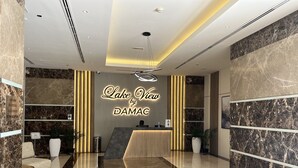 A modern hotel lobby with a reception desk, seating area, and a sign reading "Lake View by DAMAC." - HiGuests - Lake view (Dubai)