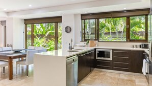 Uma cozinha moderna com ilha central, eletrodomésticos embutidos e grandes janelas com vista para um jardim tropical.