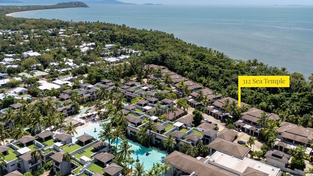 Vista aérea de um resort com várias construções tipo bangalô, uma piscina central e vista para o mar.