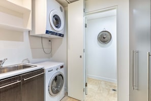 A modern laundry room with a washing machine, dryer, and a drying rack. - Seascape Holidays at Seascape Temple Beachfront Villa 312 (Douglas)