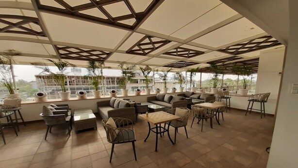 A spacious outdoor seating area with multiple sofas, chairs, and tables, surrounded by large windows and potted plants. - Hotel 18 Keys (Bhopal)