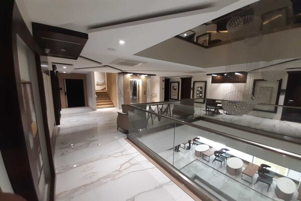 A modern hotel lobby with a marble floor, glass railing, and a staircase leading to an upper level.