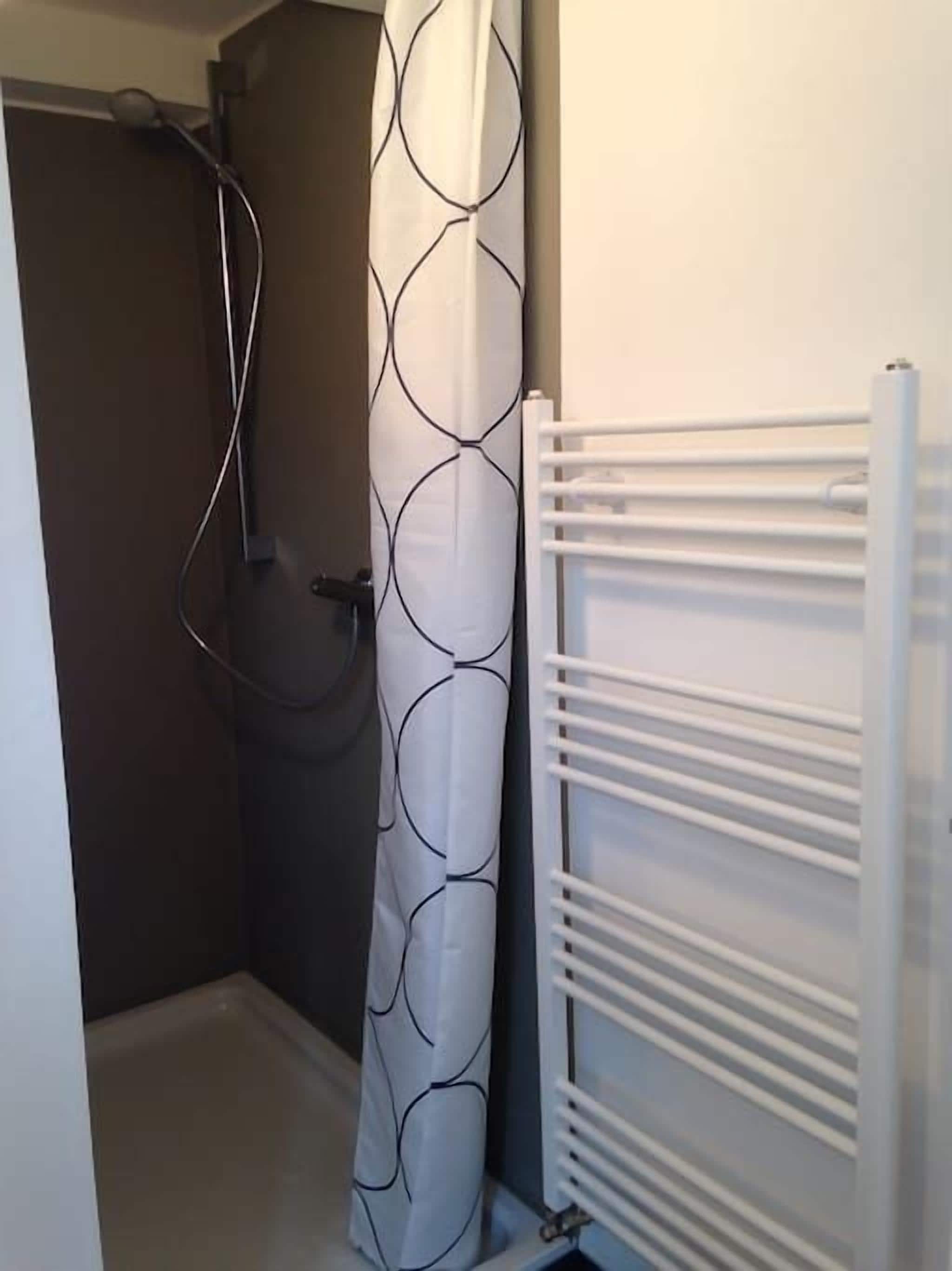 Un baño con ducha, un radiador blanco y una cortina estampada.