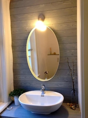 Un baño con un espejo redondo, un lavamanos blanco y una pared de madera.