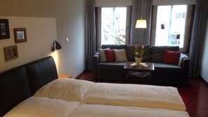 Ein Hotelzimmer mit einem großen Bett, einer Couch, einem kleinen Tisch mit Blumenvase und einem Fenster mit Vorhängen.