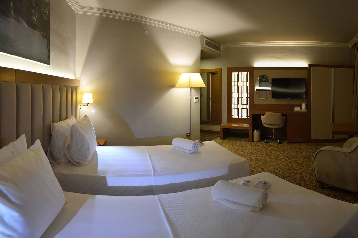 A hotel room with two beds, a desk, a chair, a TV, and a bathroom.