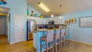A kitchen with a central island, bar stools, a microwave, and a refrigerator. - Private Pool, Pet Friendly, Golf Cart Access, Close to Beach (Port Aransas)