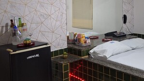 Habitación de hotel con pared de diseño geométrico, cama con ropa de cama blanca, minibar y una tira de luz roja que crea ambiente a lo largo del borde de la cama.