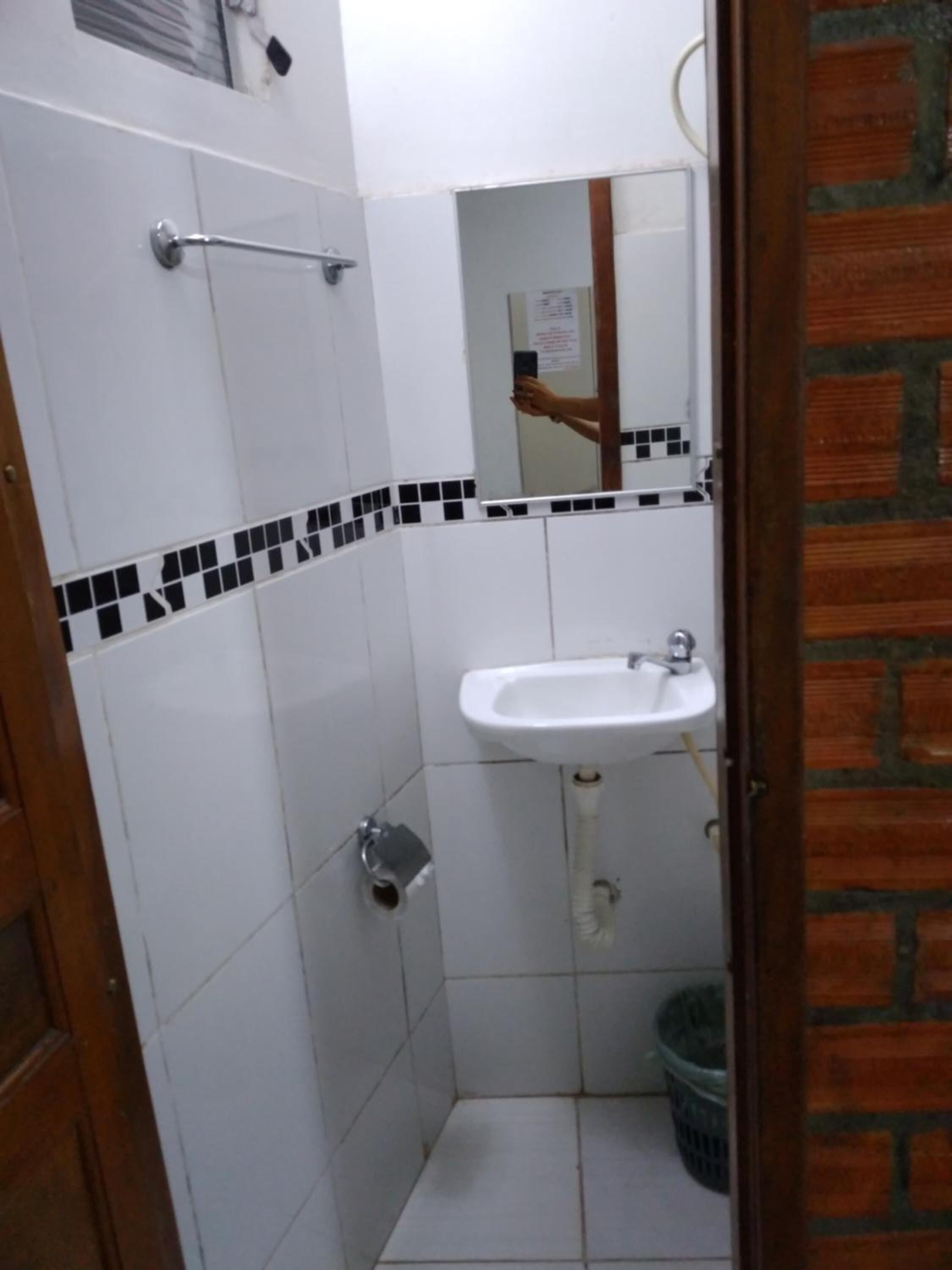 Un baño pequeño con azulejos blancos, un lavamanos blanco, un espejo y una puerta con marco de madera.
