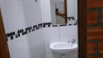 Un baño pequeño con azulejos blancos, un lavamanos blanco, un espejo y una puerta con marco de madera.