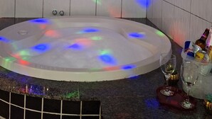 Un baño moderno con una bañera redonda grande e iluminada, paredes de azulejos y un mostrador con diversos objetos.