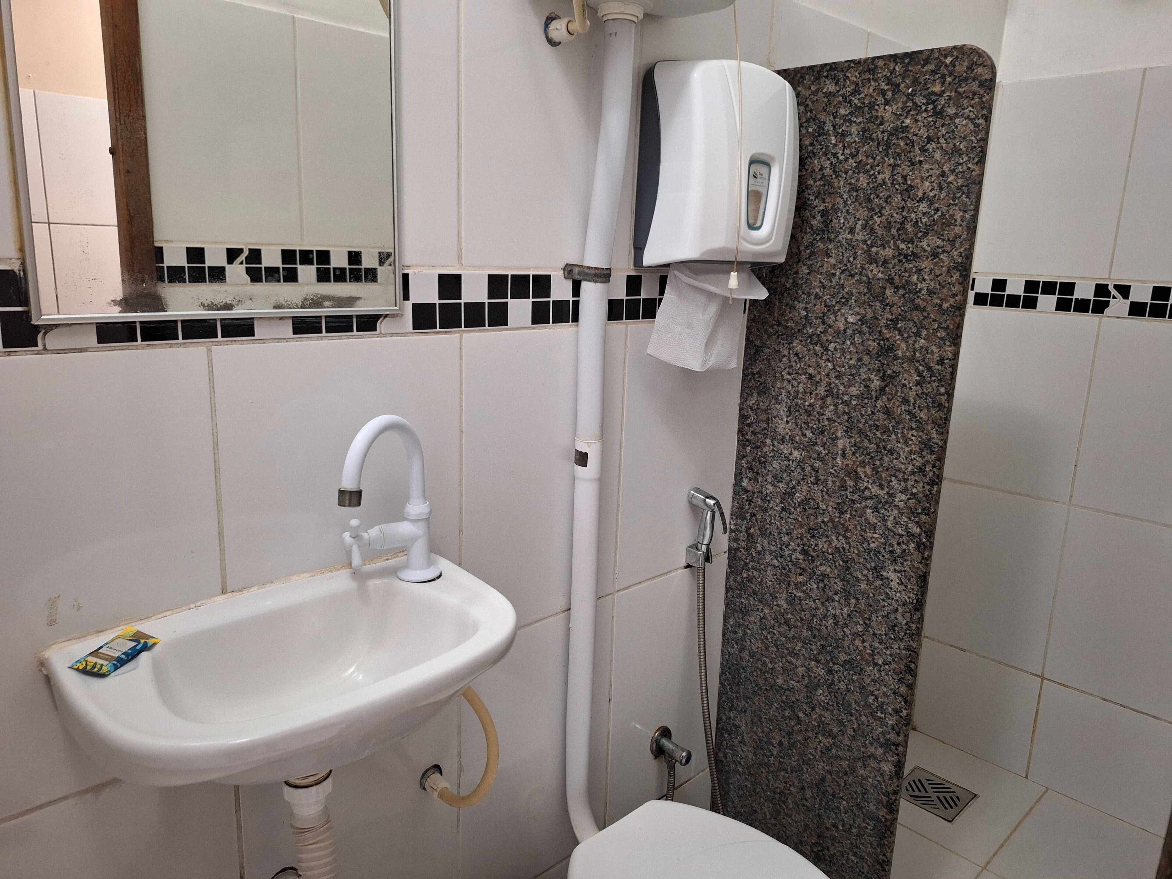 Un baño con lavamanos blanco, espejo, dispensador de jabón y zona de ducha.