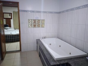 Casa de banho com uma banheira grande, paredes revestidas a azulejos e zona de duche visível.