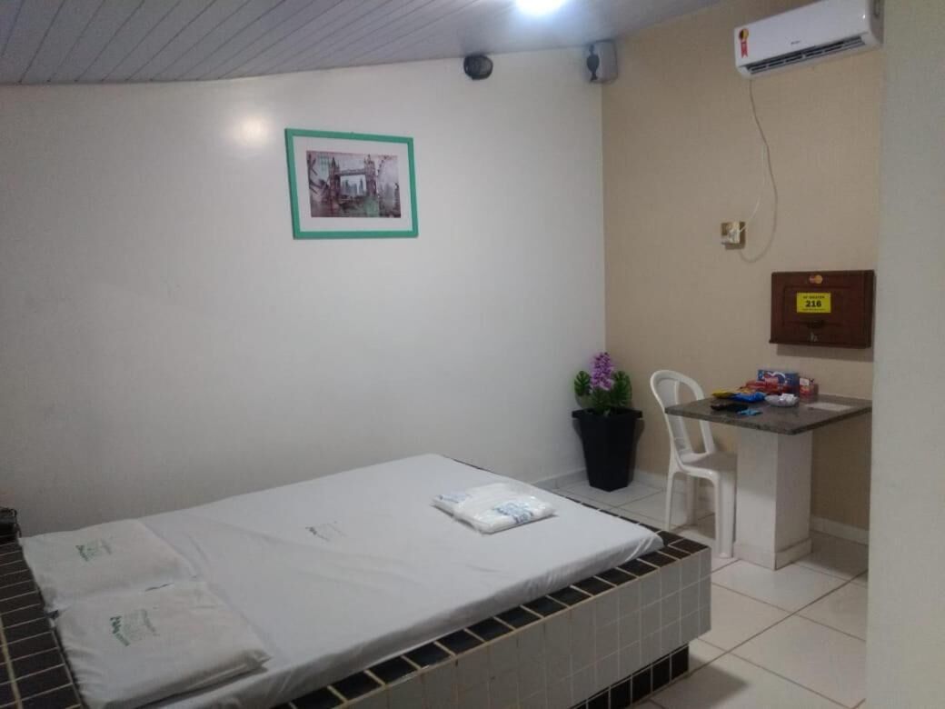 Une petite pièce propre, avec un lit simple, un petit bureau, une plante en pot et un climatiseur fixé au mur.