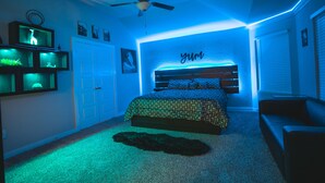 A bedroom with a bed, a ceiling fan, and a wall with a 'yum' sign.