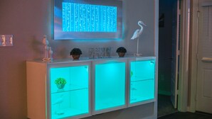 A white console with three illuminated drawers, a wall-mounted digital display, and decorative items including a bird sculpture and potted plants.