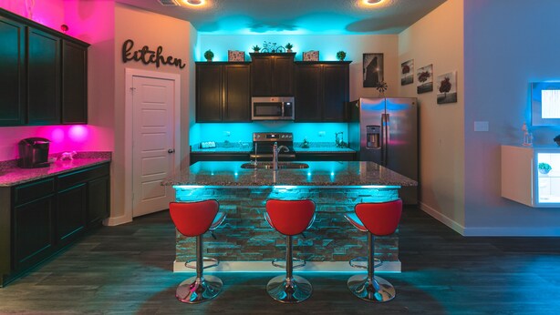 A modern kitchen with a central island, red bar stools, and a neon sign on the wall.